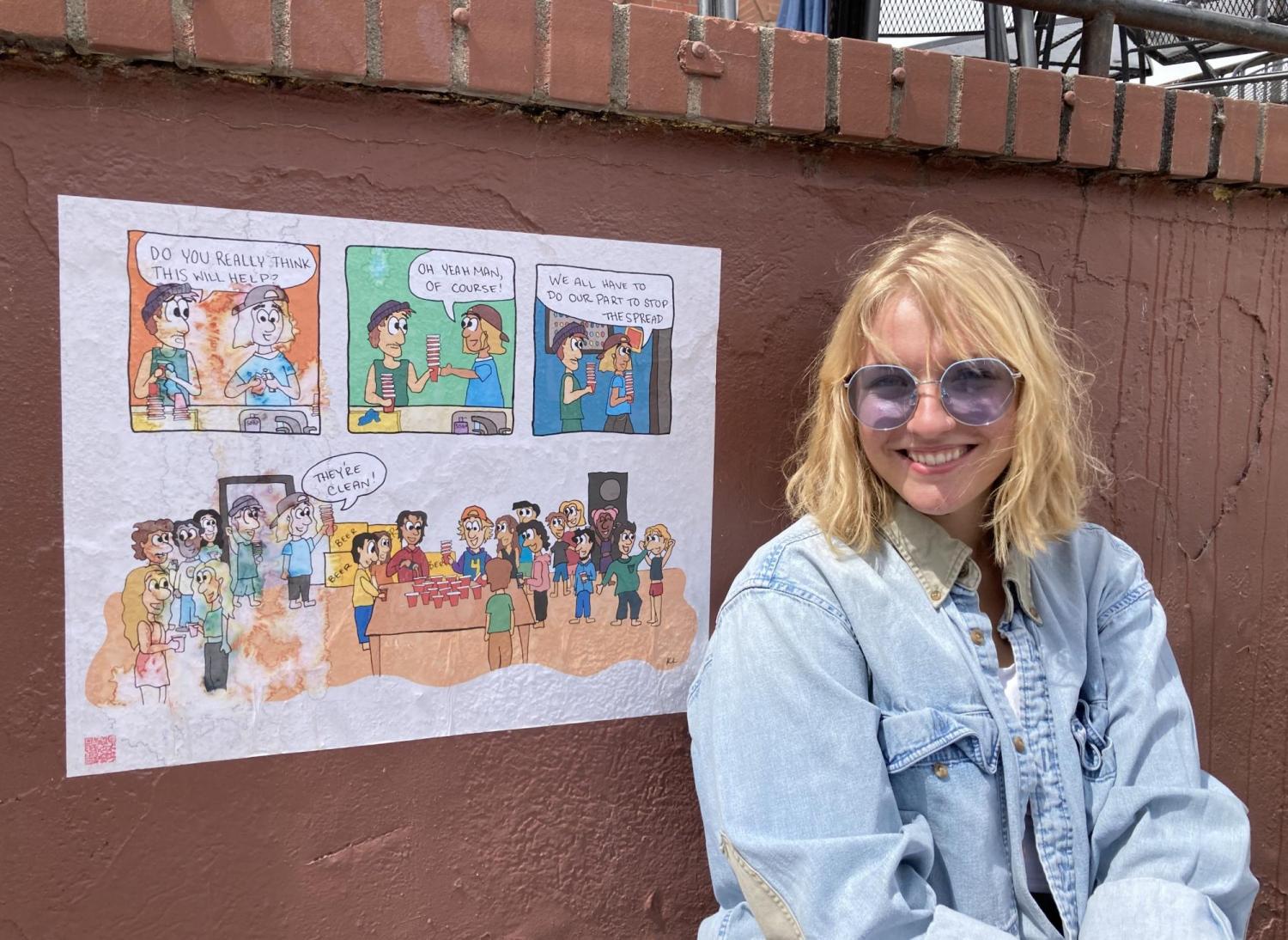 Artist standing in front of a wall where she has pasted her comic strip