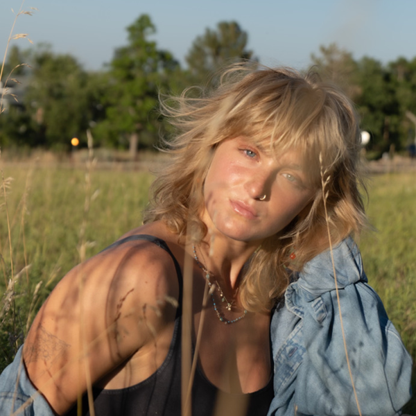 Abby Boutrous -  A person in a denim jacket poses in a field with tall grasses