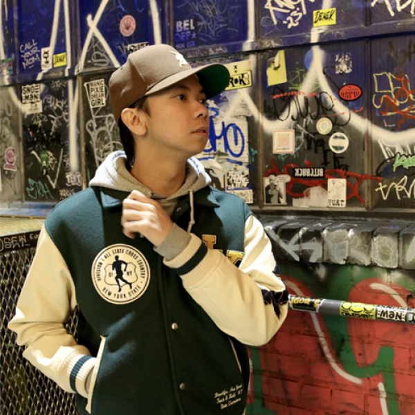 Andrew Batilo - A person in a varsity jacket stands in front of a graffiti-covered wall.