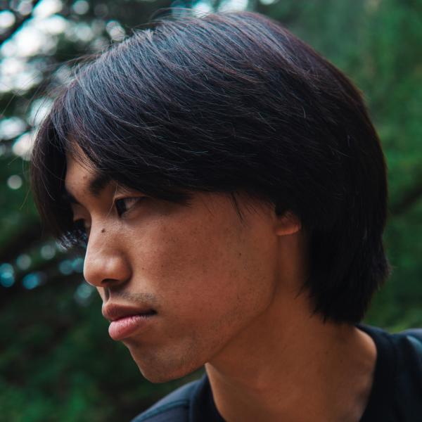 Bradyn Yonaha - A close-up side profile of a person with dark hair against a natural, leafy background.