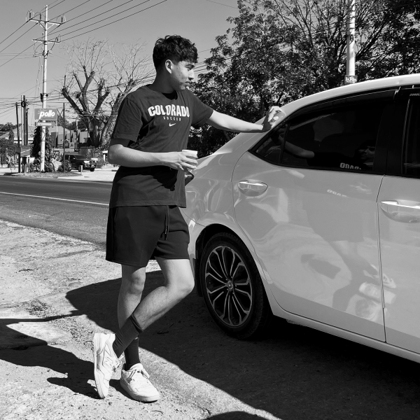 Carlos Franco - A black and white photo of a person leaning on a car, wearing shorts and a t-shirt with text