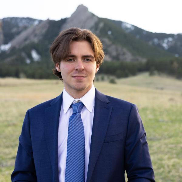 Clayton Edge - A man in a suit stands with a scenic mountain backdrop.