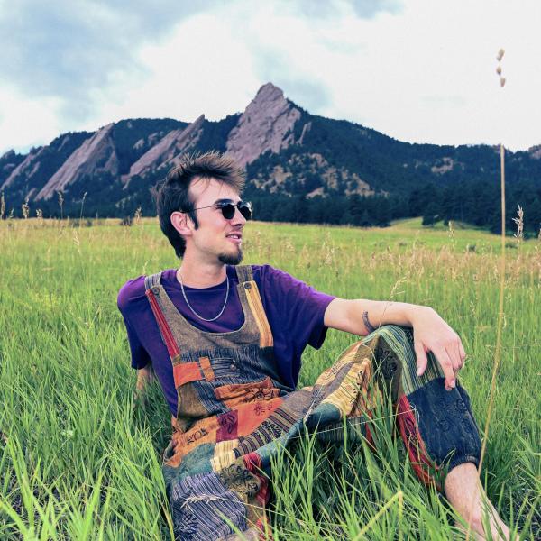 man in colorful clothes sitting in grass in front of mountains