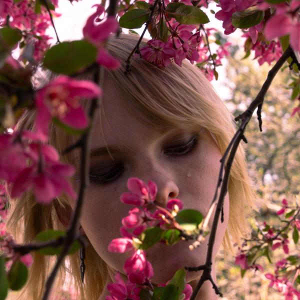 eruchan - A close-up of a person's face partially obscured by pink blossoms in the foreground.