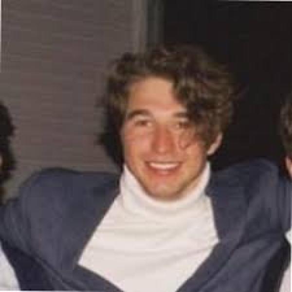 Jack Dobson - A person with a warm smile wearing a blue suit and a white turtleneck.