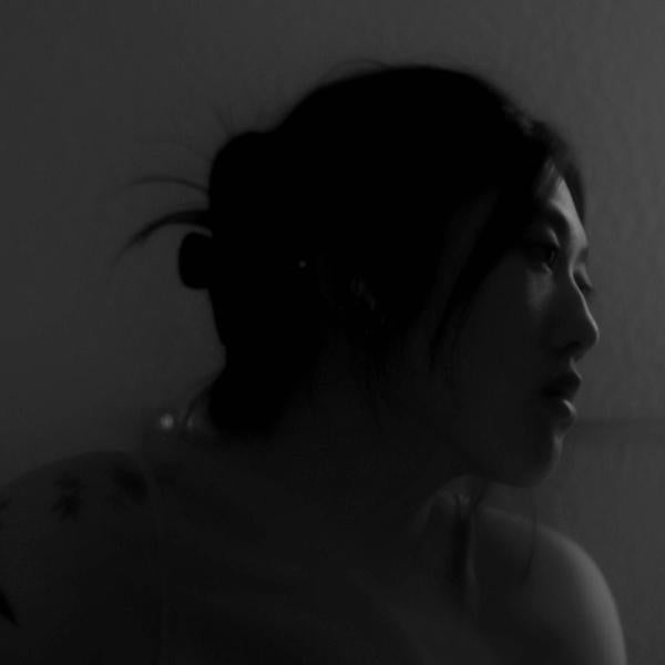 LisaAn -A low-light profile image of a person with a visible tattoo on the shoulder looking to the side.