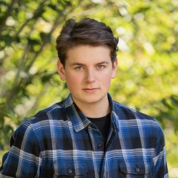 Tyler Hess - A person in a blue and black plaid shirt posing with a natural green background