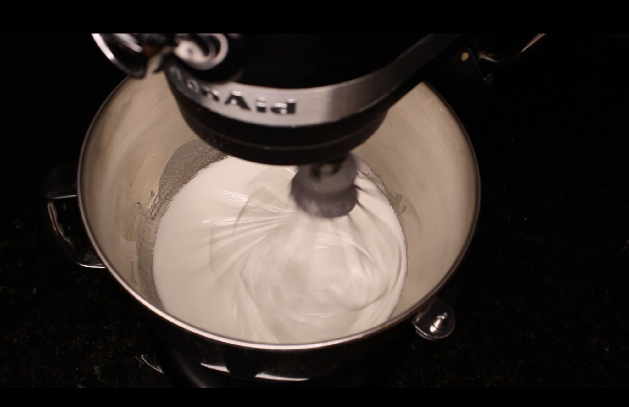 Above shot of a KitchenAid Mixer, in the mixing bowl contains flour, oil, and eggs unmixed.