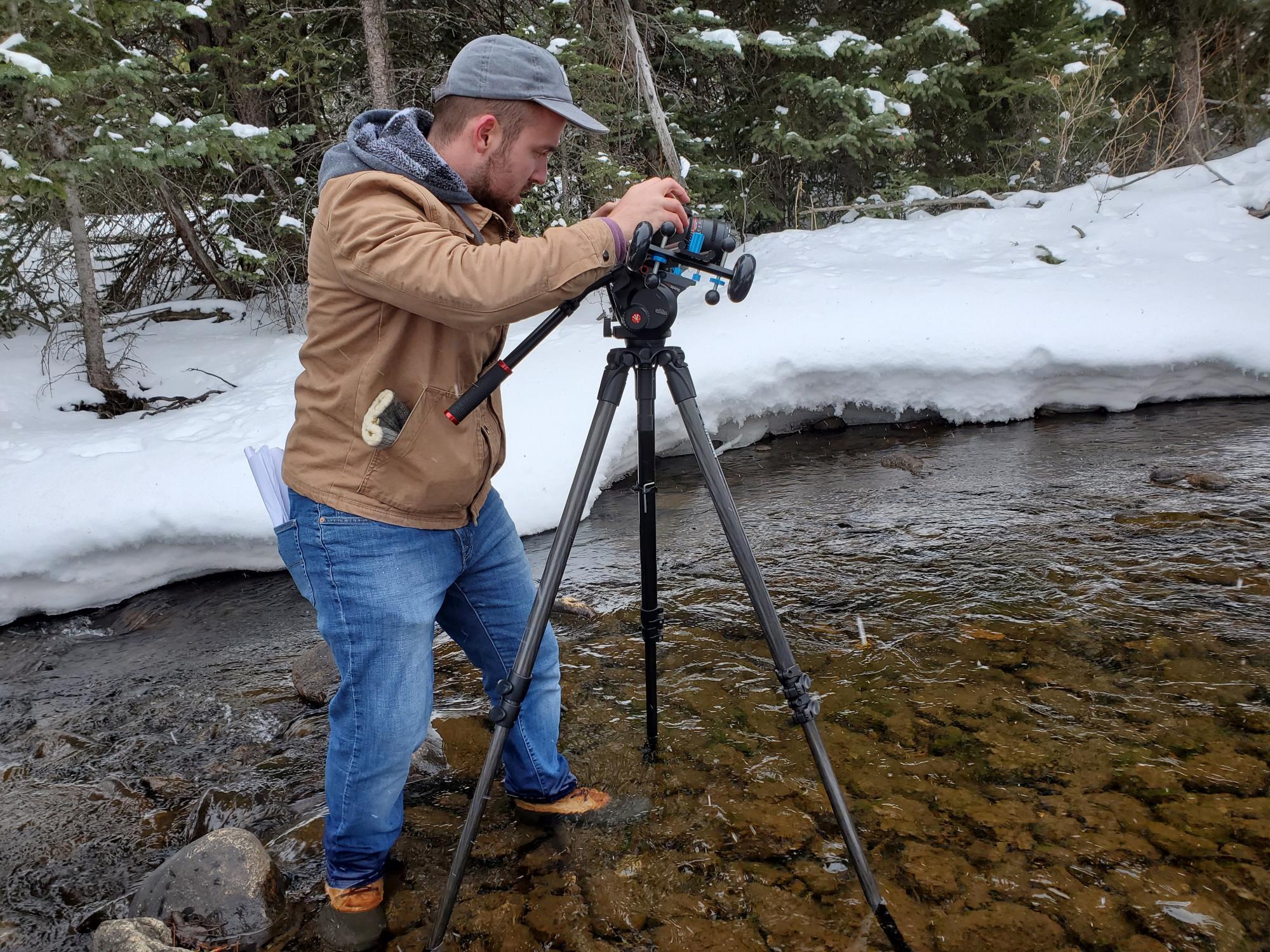 Behind the scenes camera-person standing in a creek with camera