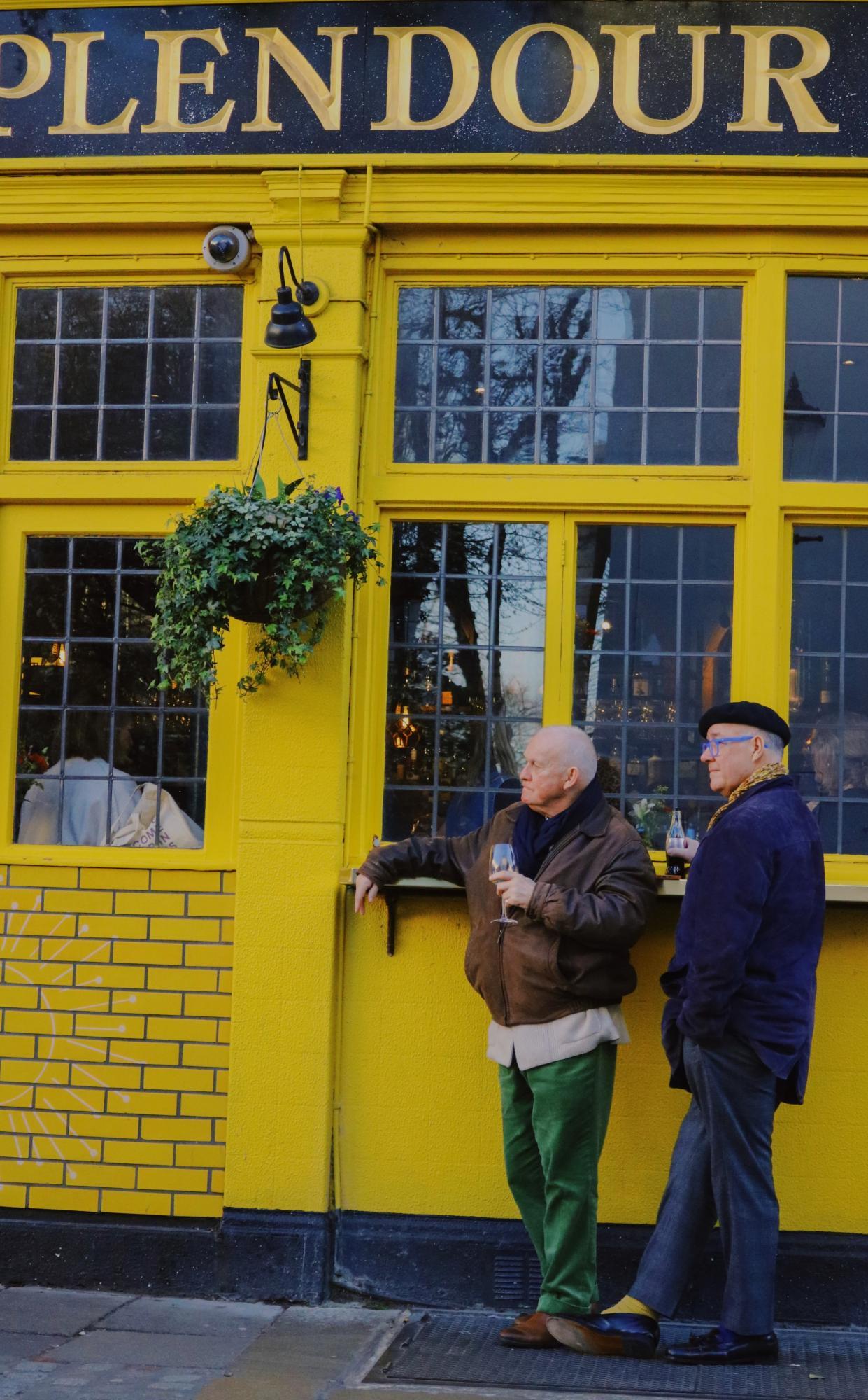 Two dapper gentlemen enjoy some beverages outside of a pub in London, England.
