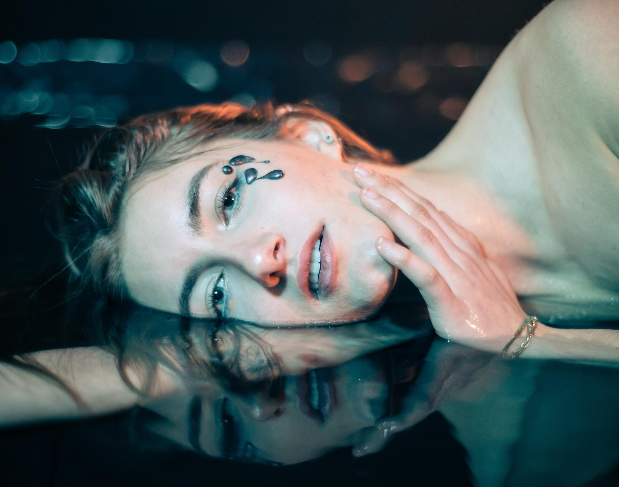 Female model with face submerged horizontally in water with cyan and orange lighting
