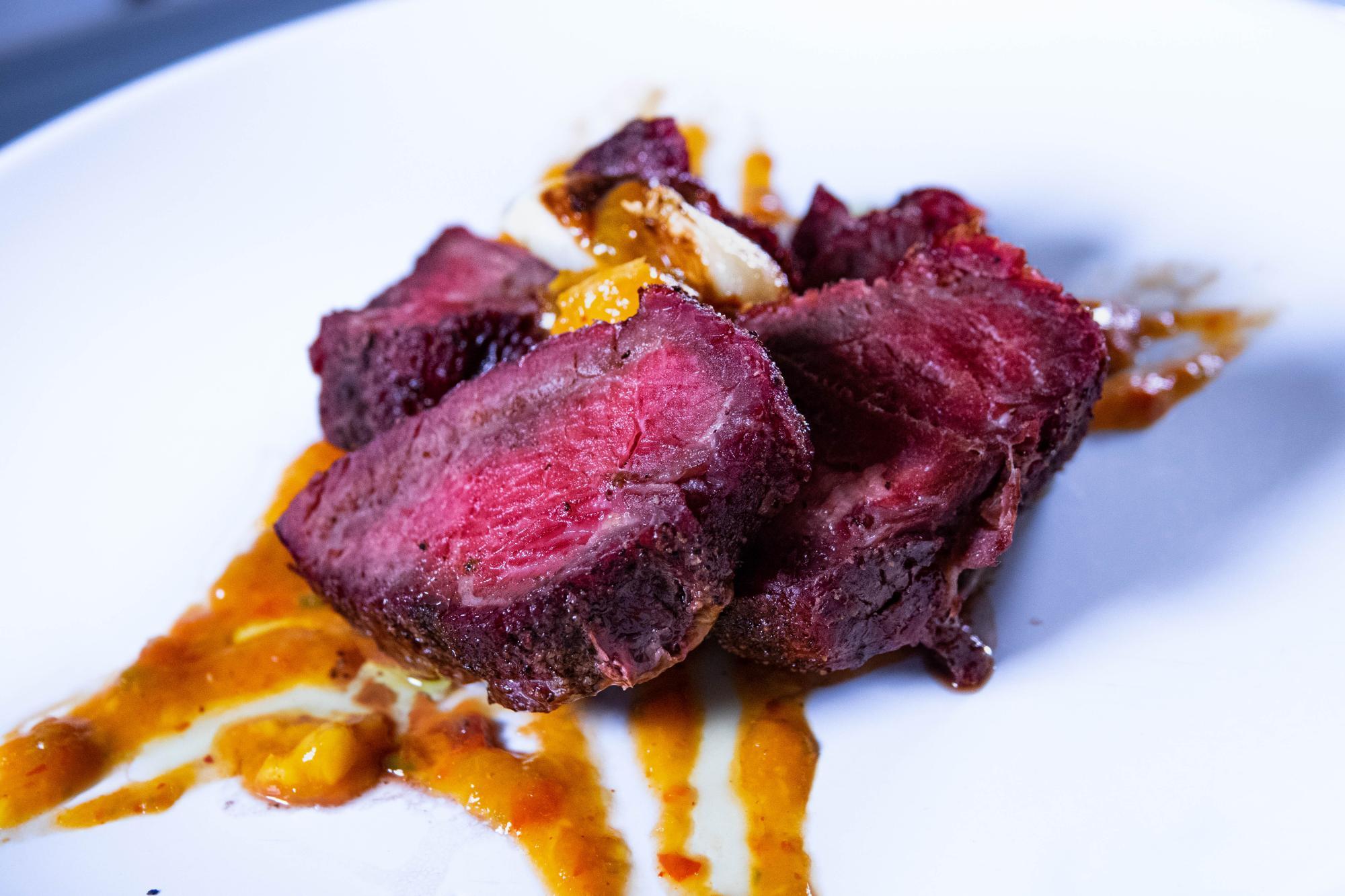 A close-up of steak on a plate with orange sauce