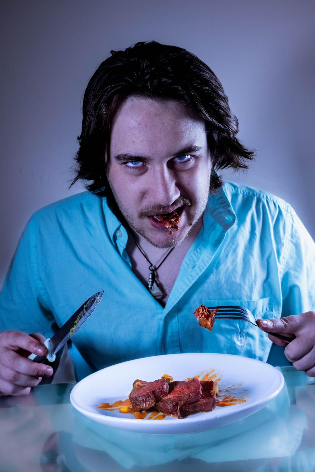 A man stares into the camera while eating steak