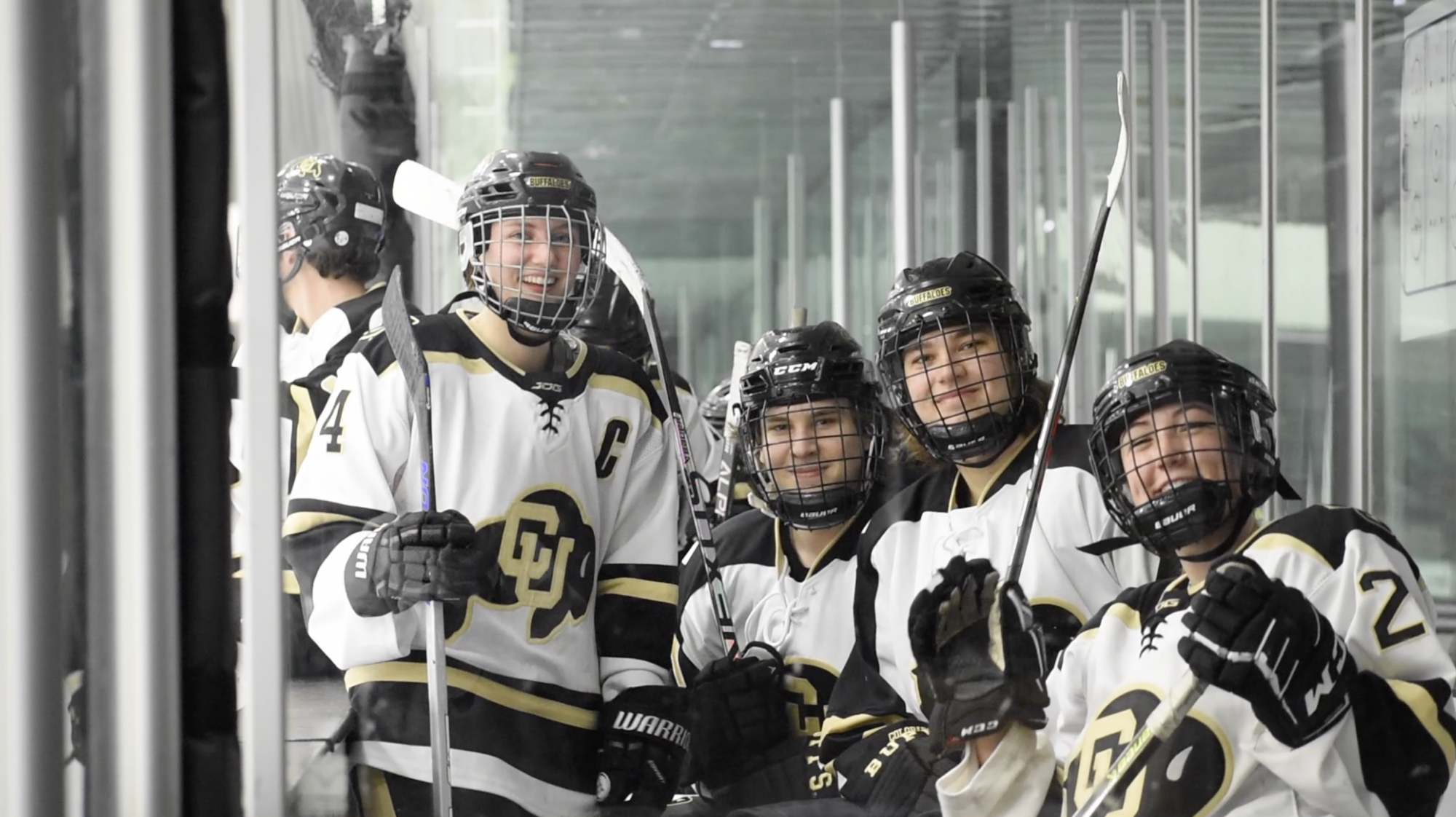 Four hockey players smiling at the camera while on the bench