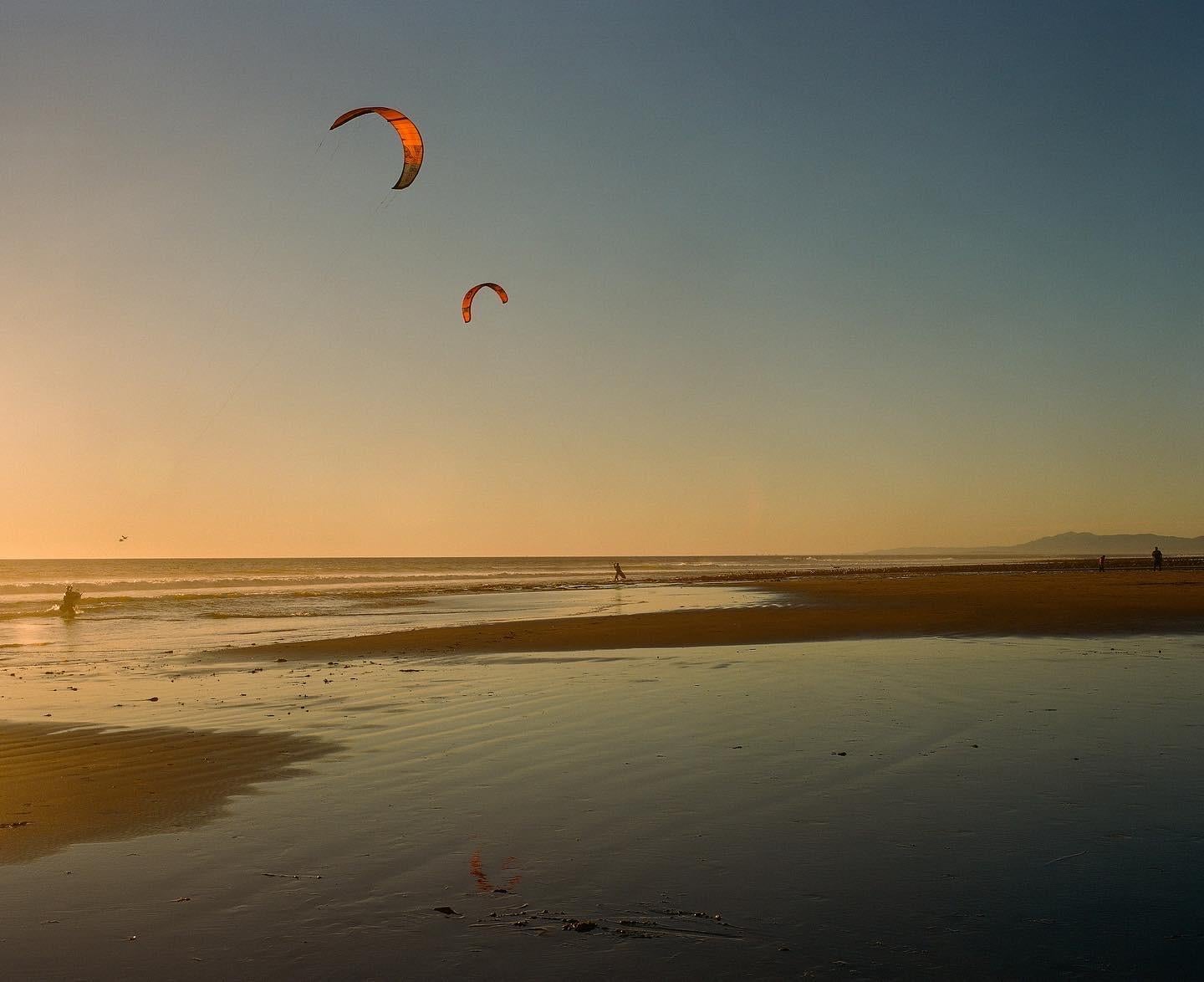 Two kite surfers struggle to get a hold of their kites on the golden beach