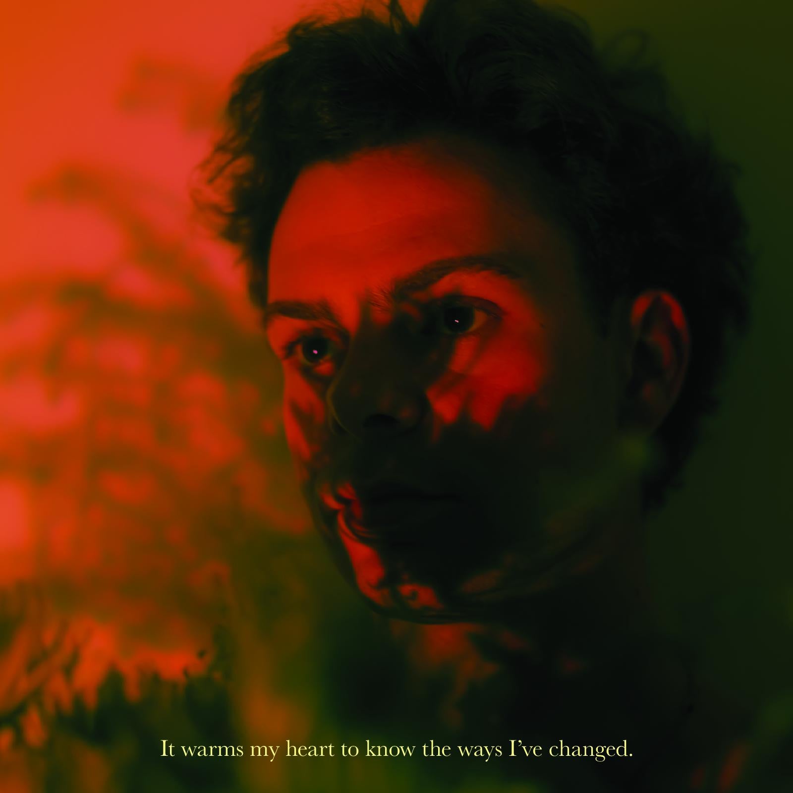 Close up portrait of Drew Hersch, slightly blurred and covered with floral textures and shadows. Dim, muted red & green lighting. In a serif typeface colored pale yellow, "It warms my heart to know the ways I've changed." This is a standout lyric from "Growing Pains".
