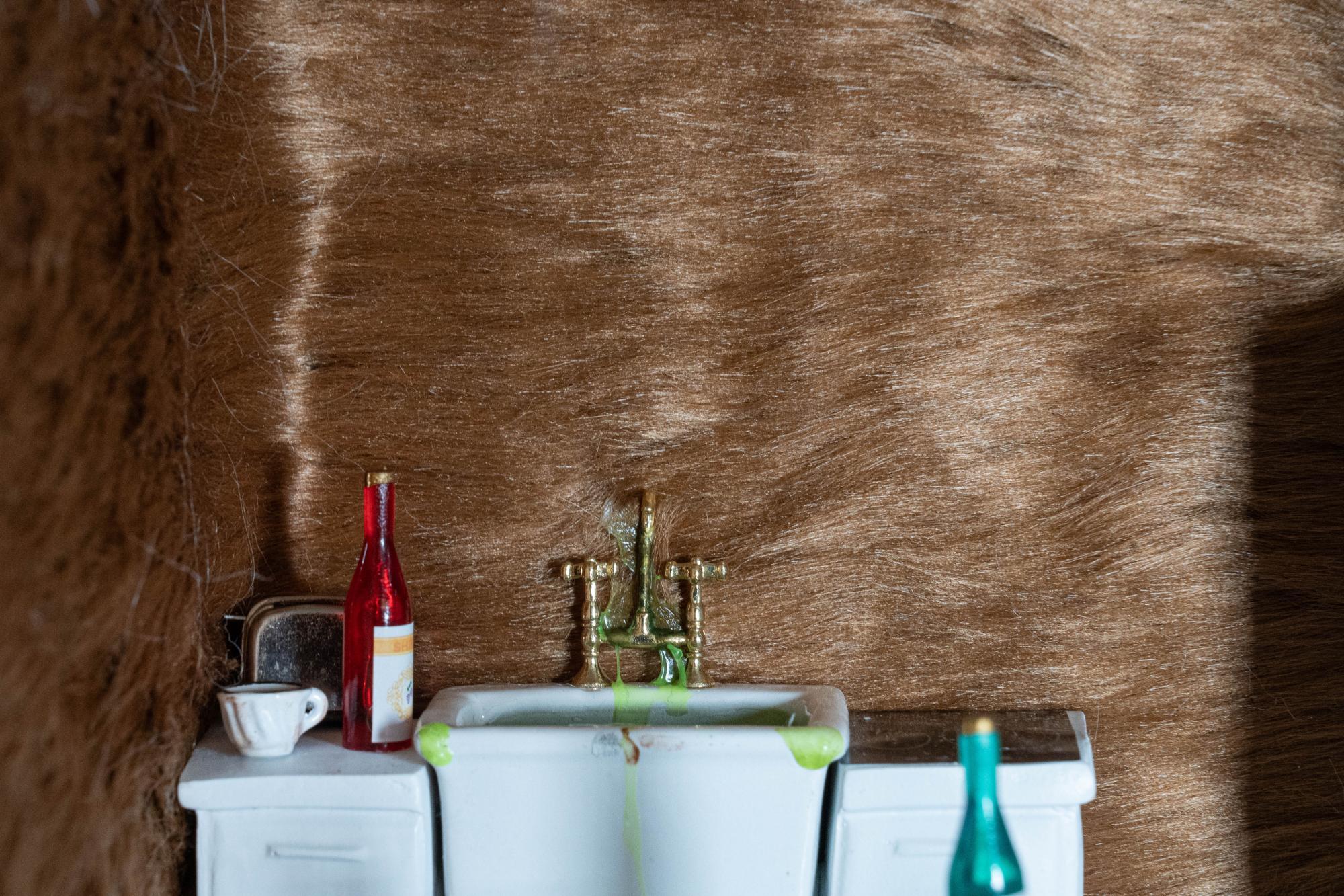 Close up of the sink in the kitchen, there is green goo coming out of the sink and stuck in the fur that is covering the walls