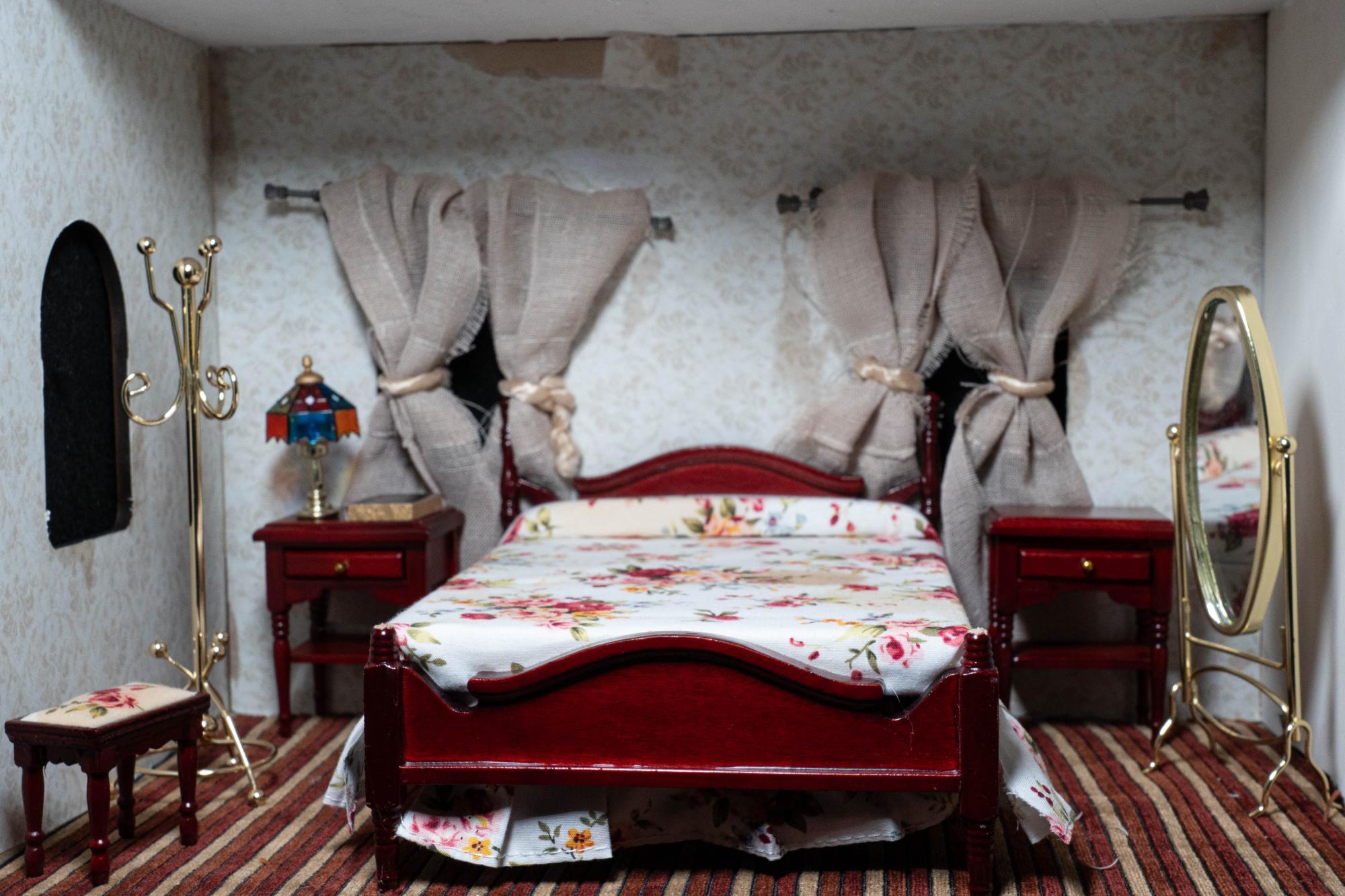 Full shot of motel room with a stained floral bedspread and maroon and gold striped carpeting