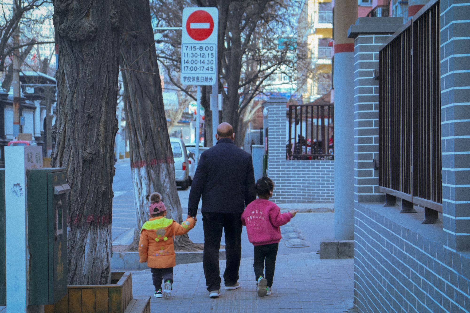 Two children hold and adults hand while walking down a street