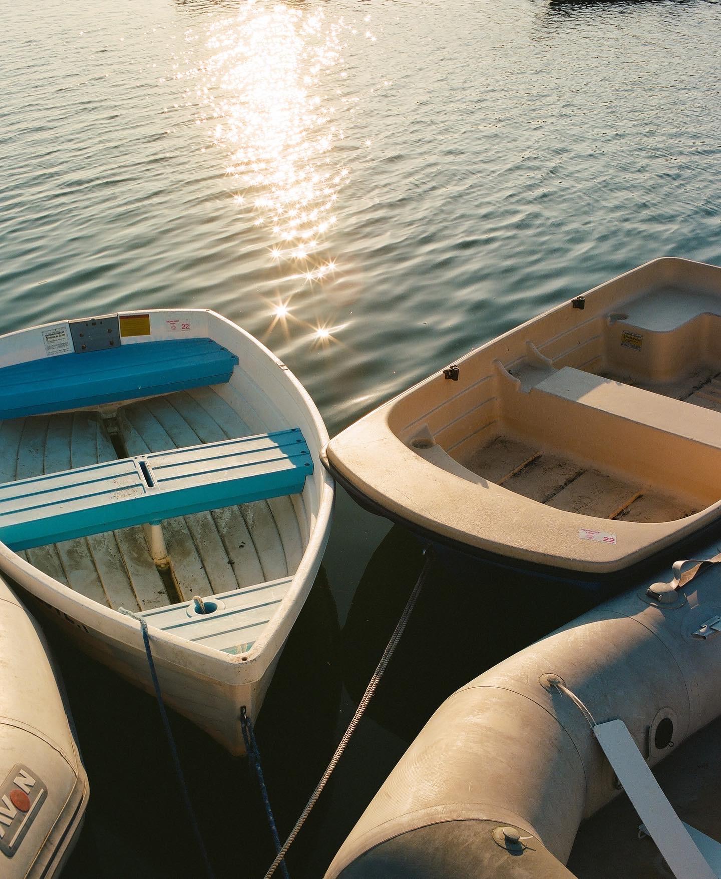 Four boats sit tied to the dock as the day breaks, and the sun dances across the calm water as it sets
