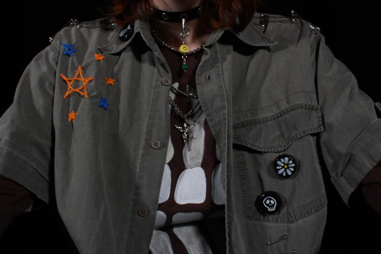 up close photo of details of outfit. orange and blue stars in top left shirt corner, daisy and skull pins on right side pocket