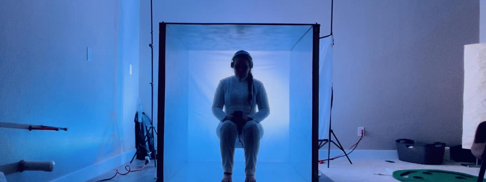 woman sitting in a box with blue light behind her