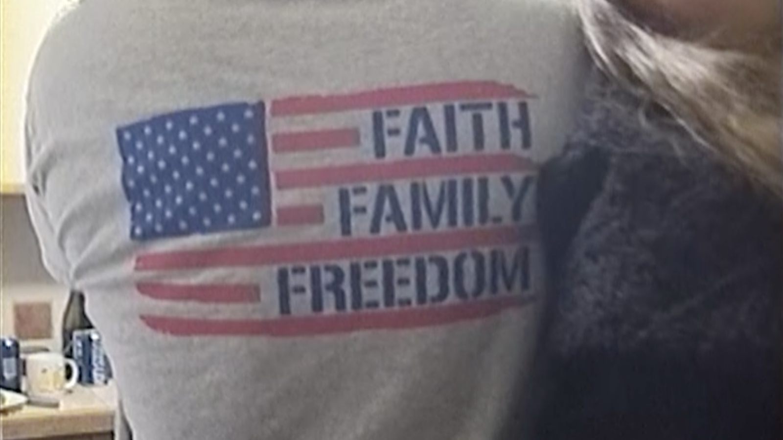 Back of someone's shirt at a party, reads "FAITH FAMILY FREEDOM" surrounded by American flag.