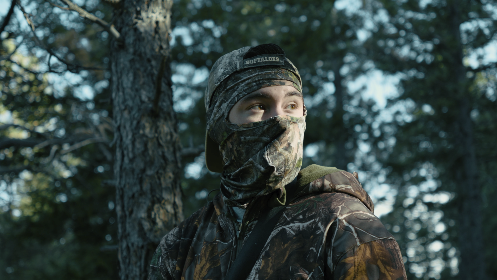 Angus wearing full camouflage in the woods looking off into distance, late afternoon