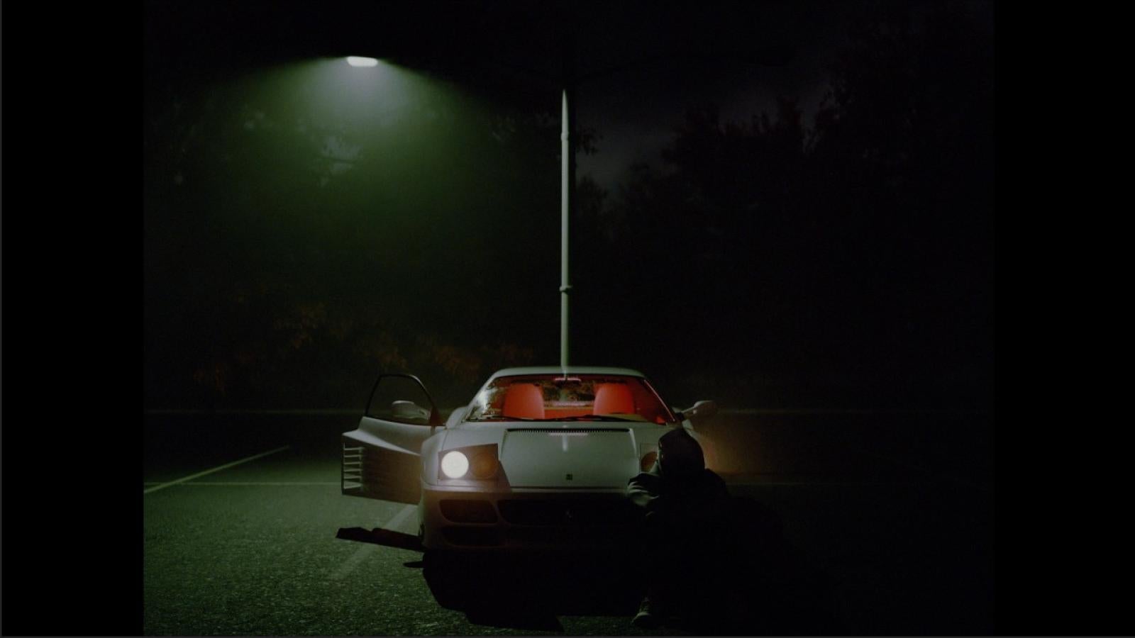 Shot of main character alone on the right side of the car. Left car door is opened. Right street light is broken.