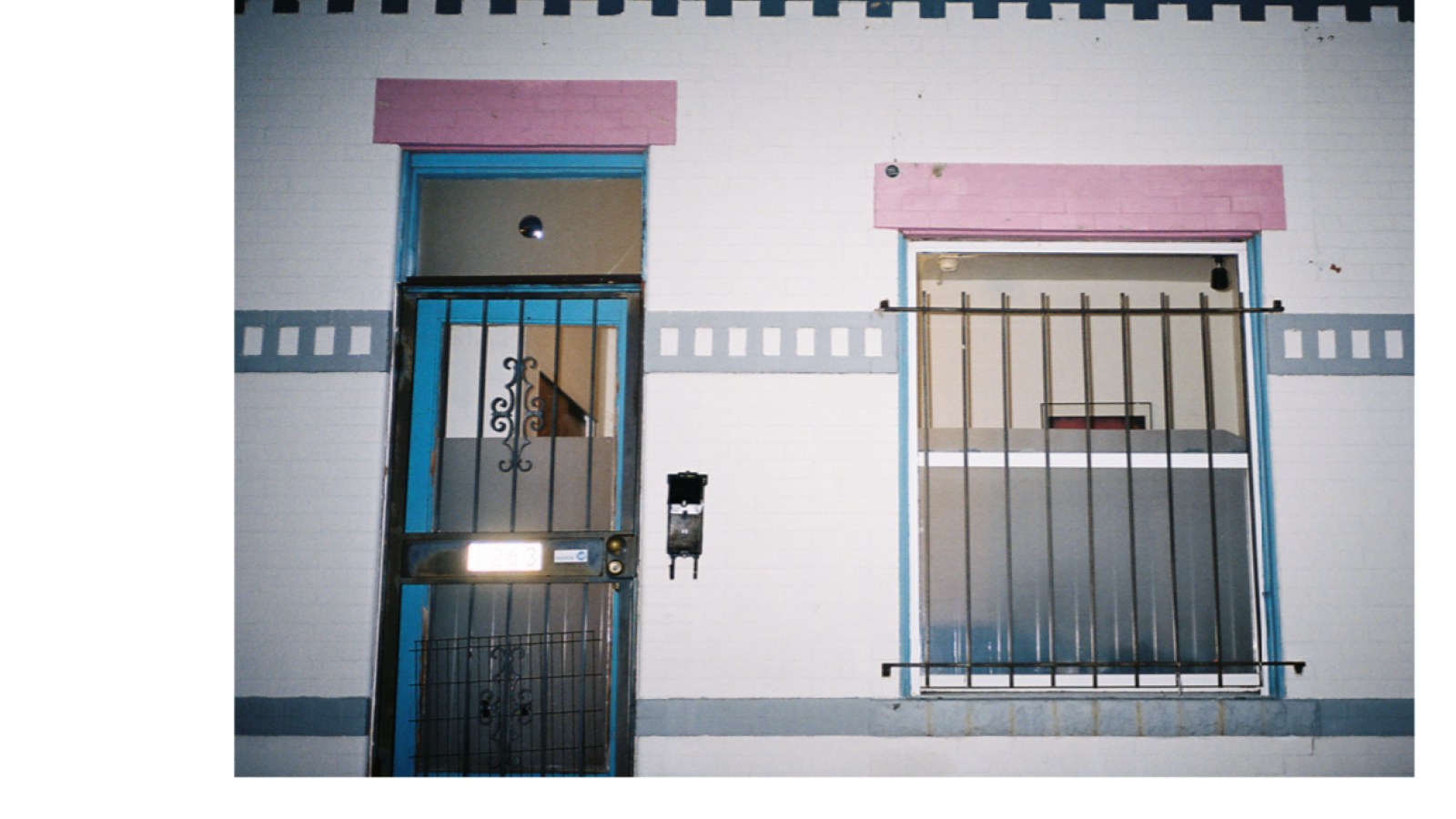 a film image of the side of a building. The paint on the building is pink, blue and white.