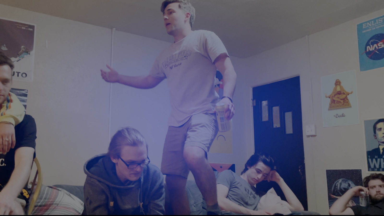 Five people in a living room, one is standing on table holding a beverage