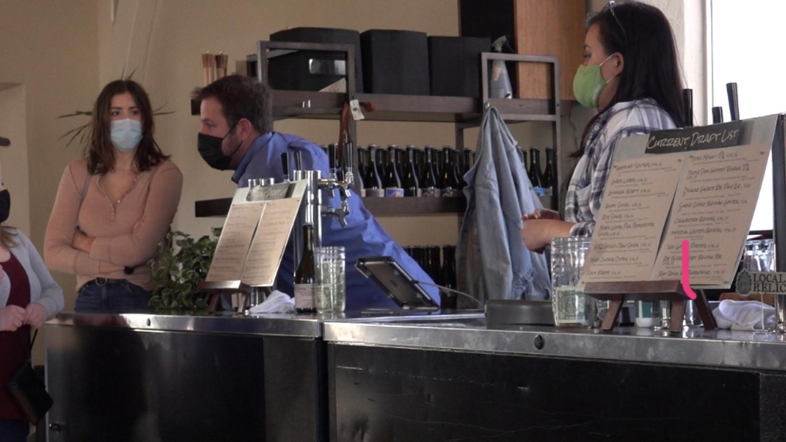 People wearing masks discussing behind a bar