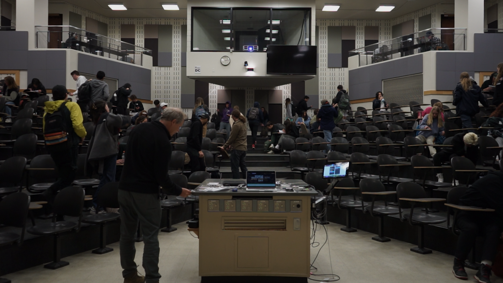 A large, crowded lecture hall begins clearing out at the end of a class.