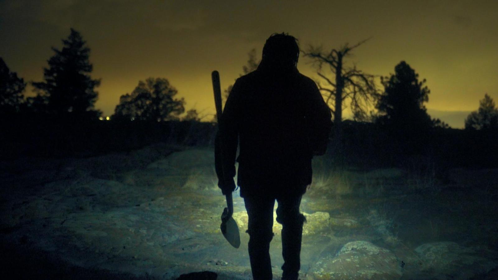 A man holding a shovel walks through the wild at Night