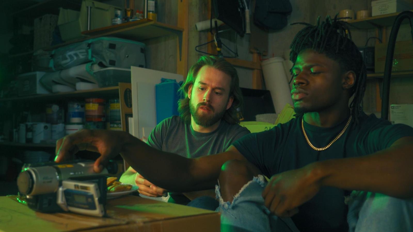 2 friends watch a camcorder in a dark basement
