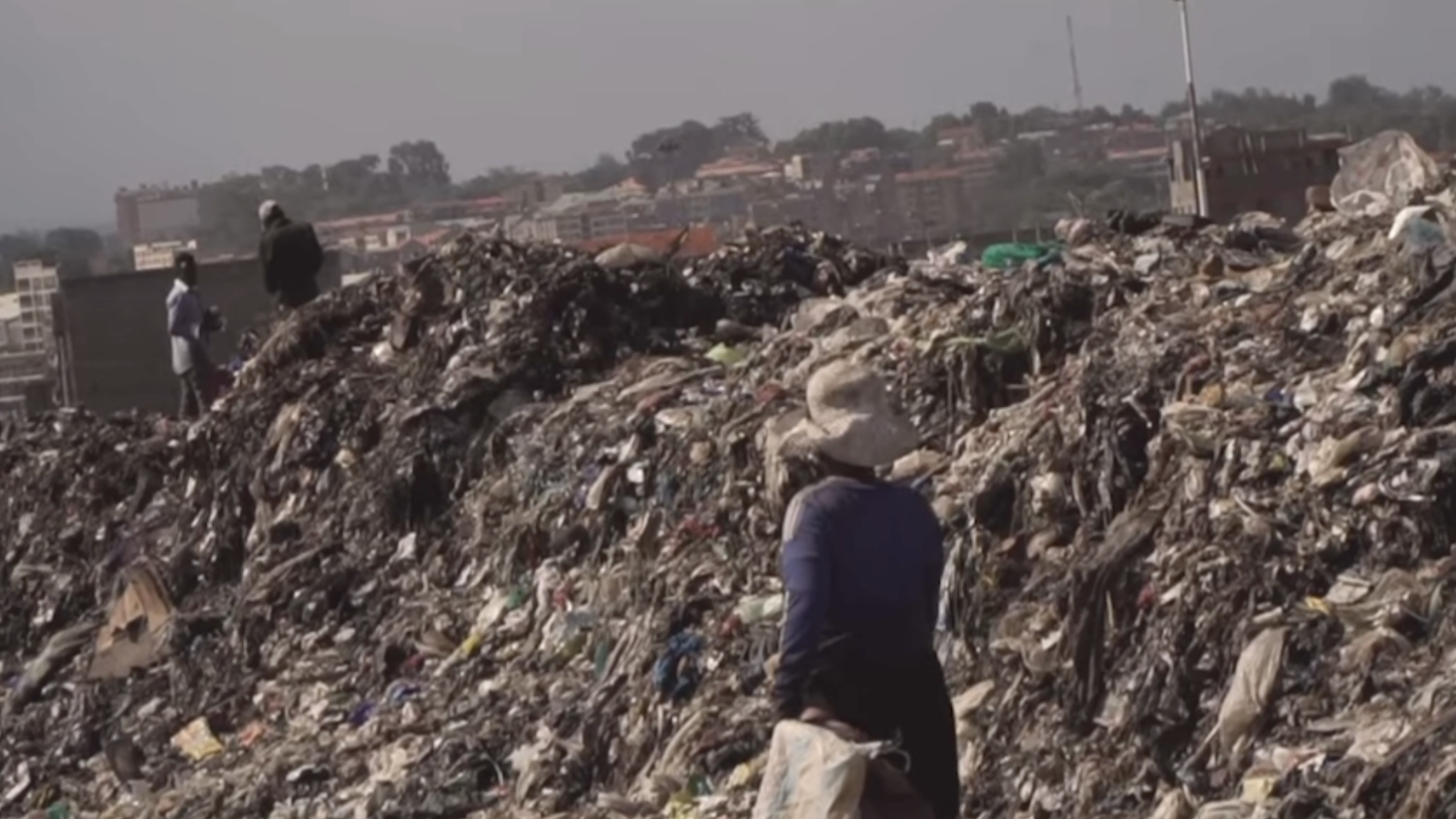 Aa woman walking alongside a very large pile of material waste.