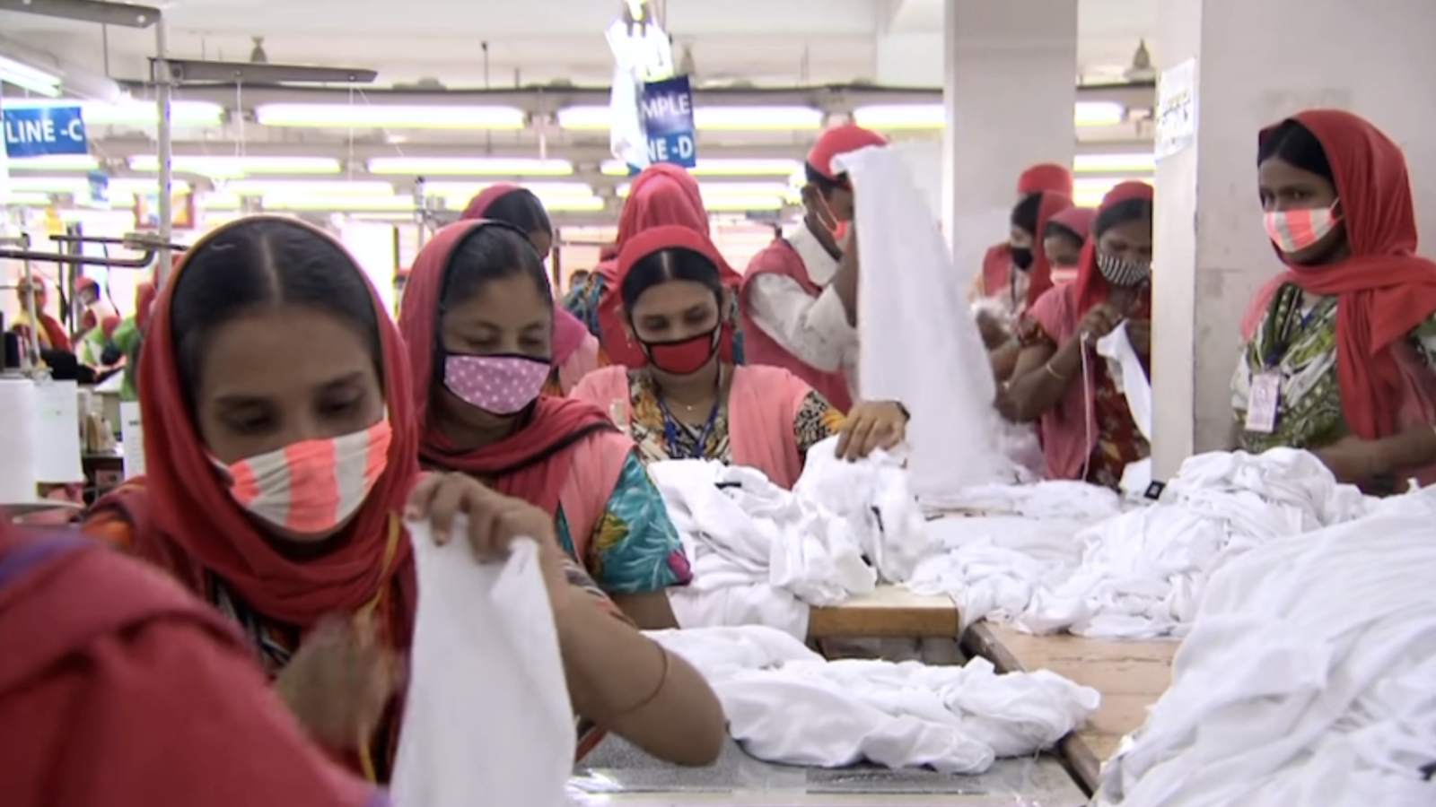 This image showcases a woman working in a clothing factory. The women in the photo are sorting through white sheet-like material.