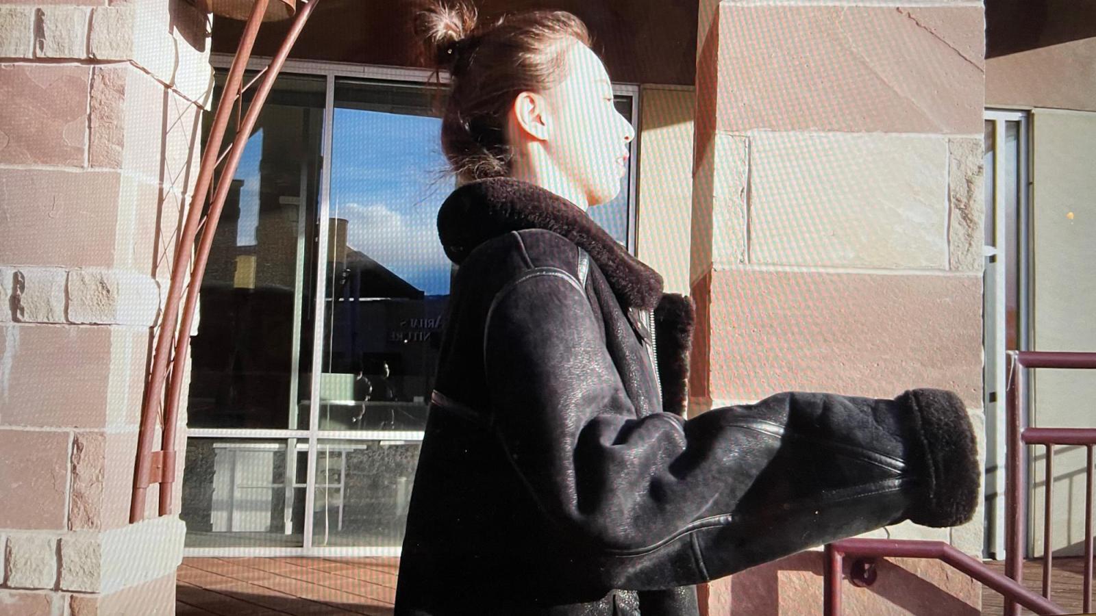 Person in a black coat in front of a store looking into the sun