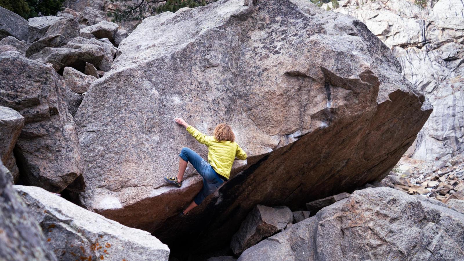 Wide angle shot of climber in blue pants and green jacket pulling himself over a ledge