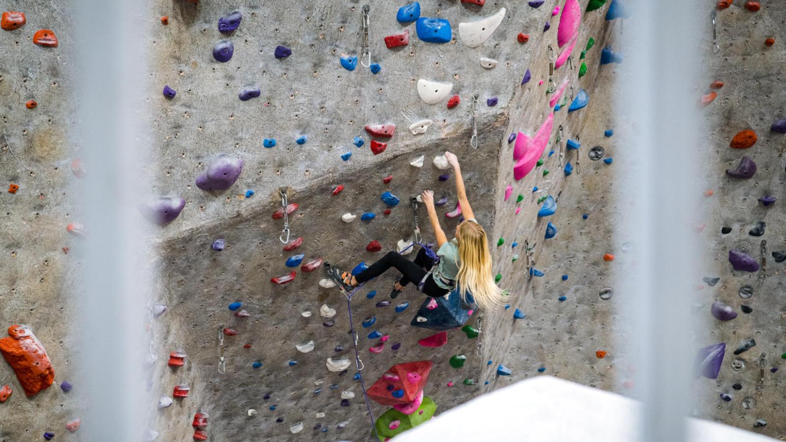 Young Girl with long hair sport climbing at the Boulder Rock Club, shot through blurred white railing
