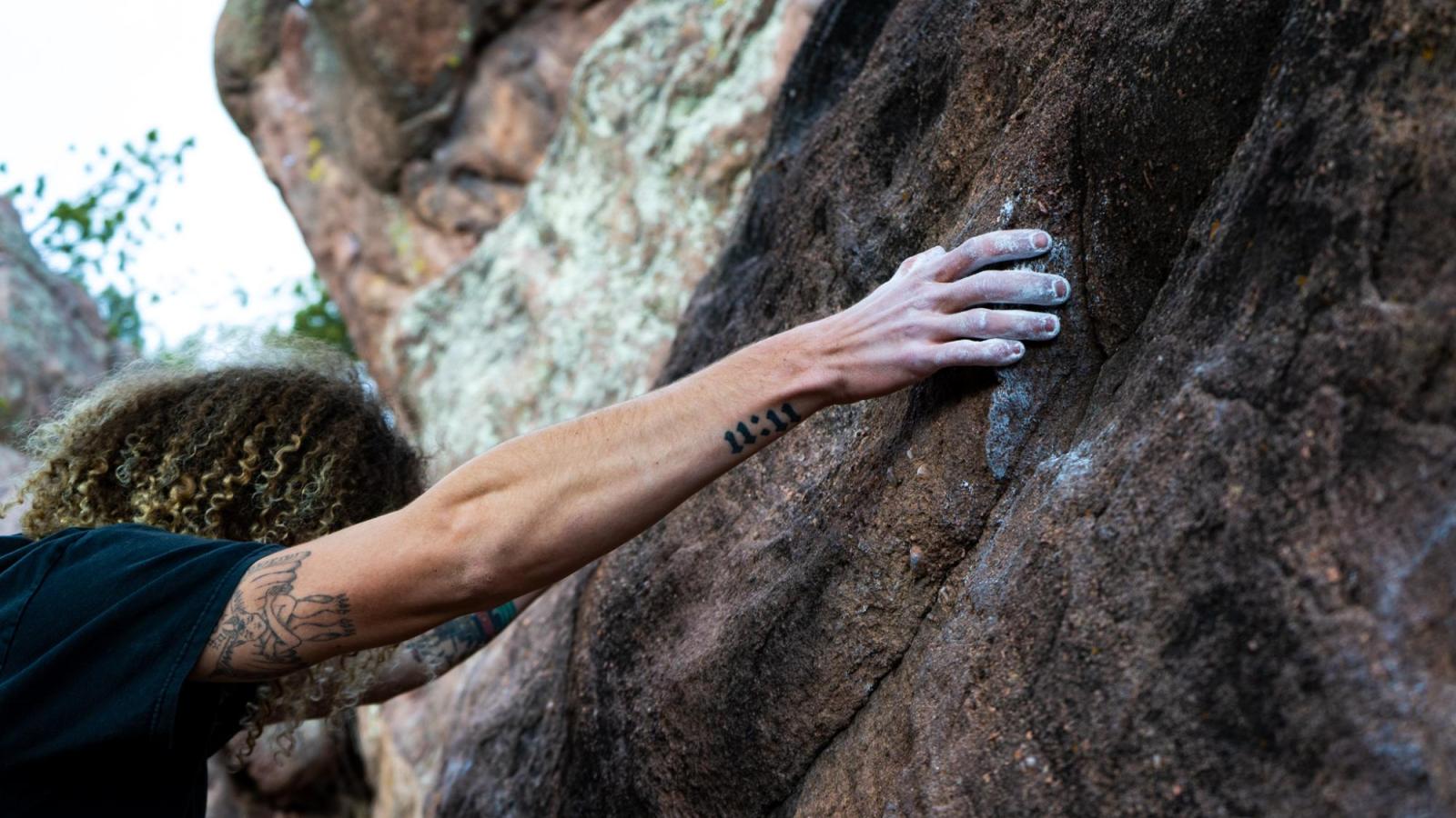 Close up of chalk covered hand on tattooed climber looking down