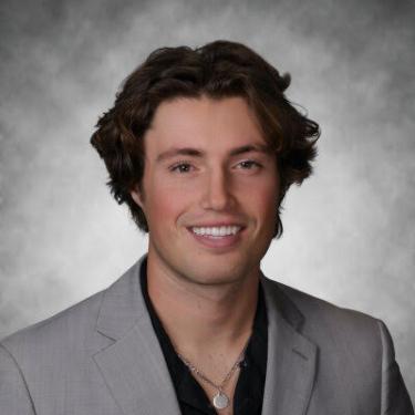 Man in a suit smiling in front of a grey background