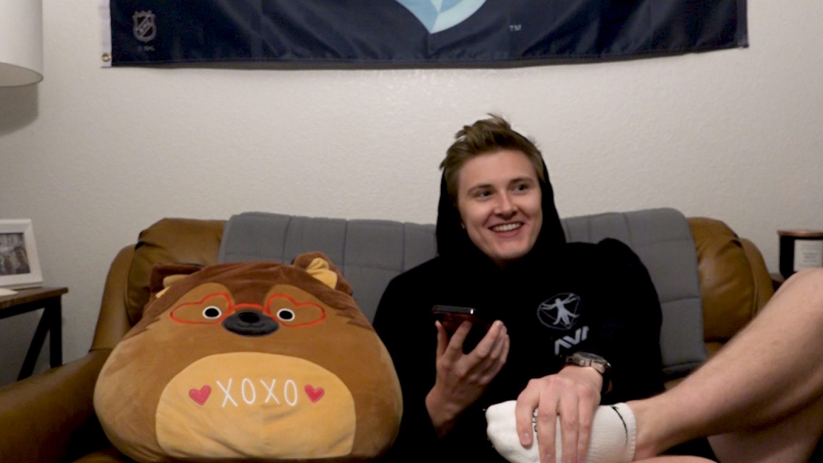 Austin Calls an Old Friend: A smiling Austin sits on his couch with his stuffed animal friend. He is calling his friend, Erin.