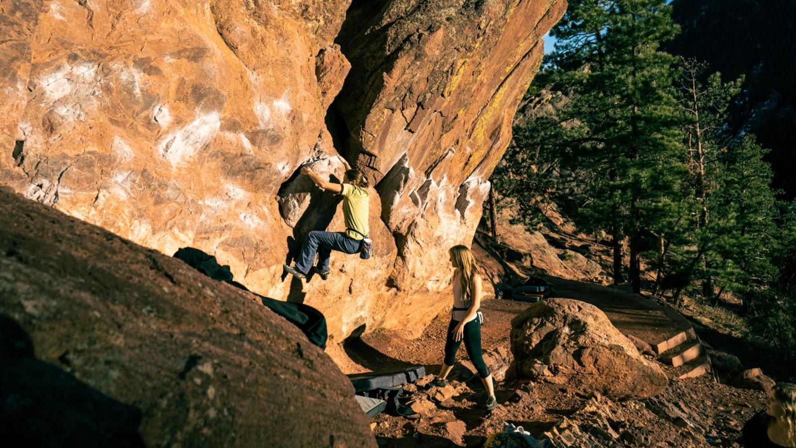 Golden hour shot of female climber in green struggling to hold on as her friend watches from behind