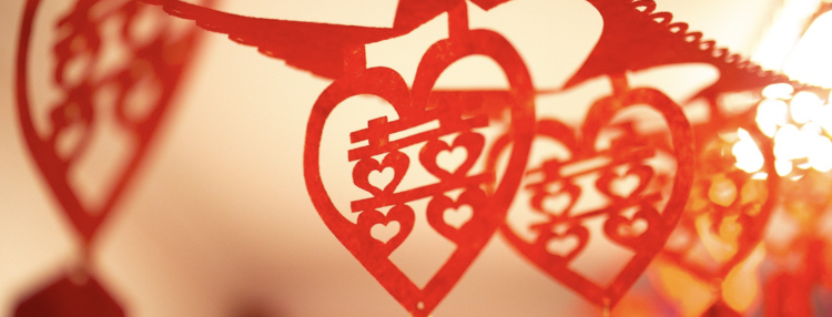 Red paper heart decorations with cut-out designs hanging in a row with a warm backlight.
