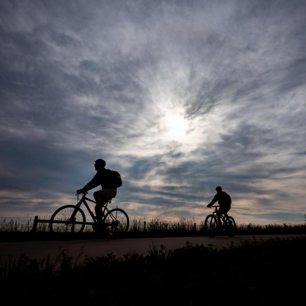 Three silhouettes of people biking in front of a cloudy sky