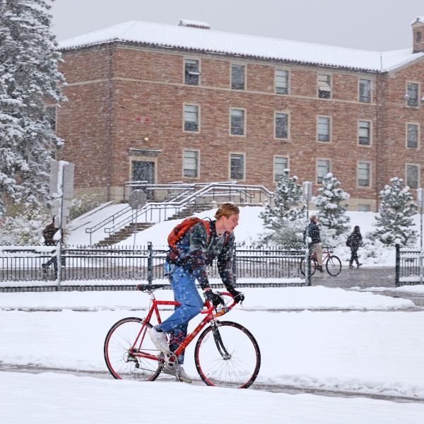 Student biking on CU campus during the first snowstorm of 2024