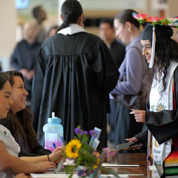 A graduating student talking with two other students at a table for the 2024 Spring Commencement Ethnic Studies Recognition Ceremony.