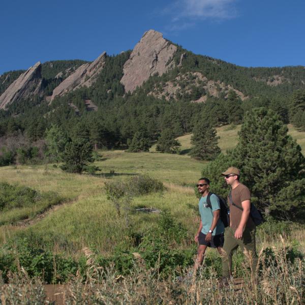 Two people hiking in Chautauqua with the Flatirons in the background