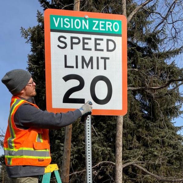 Worker installs a Vision Zero street sign.
